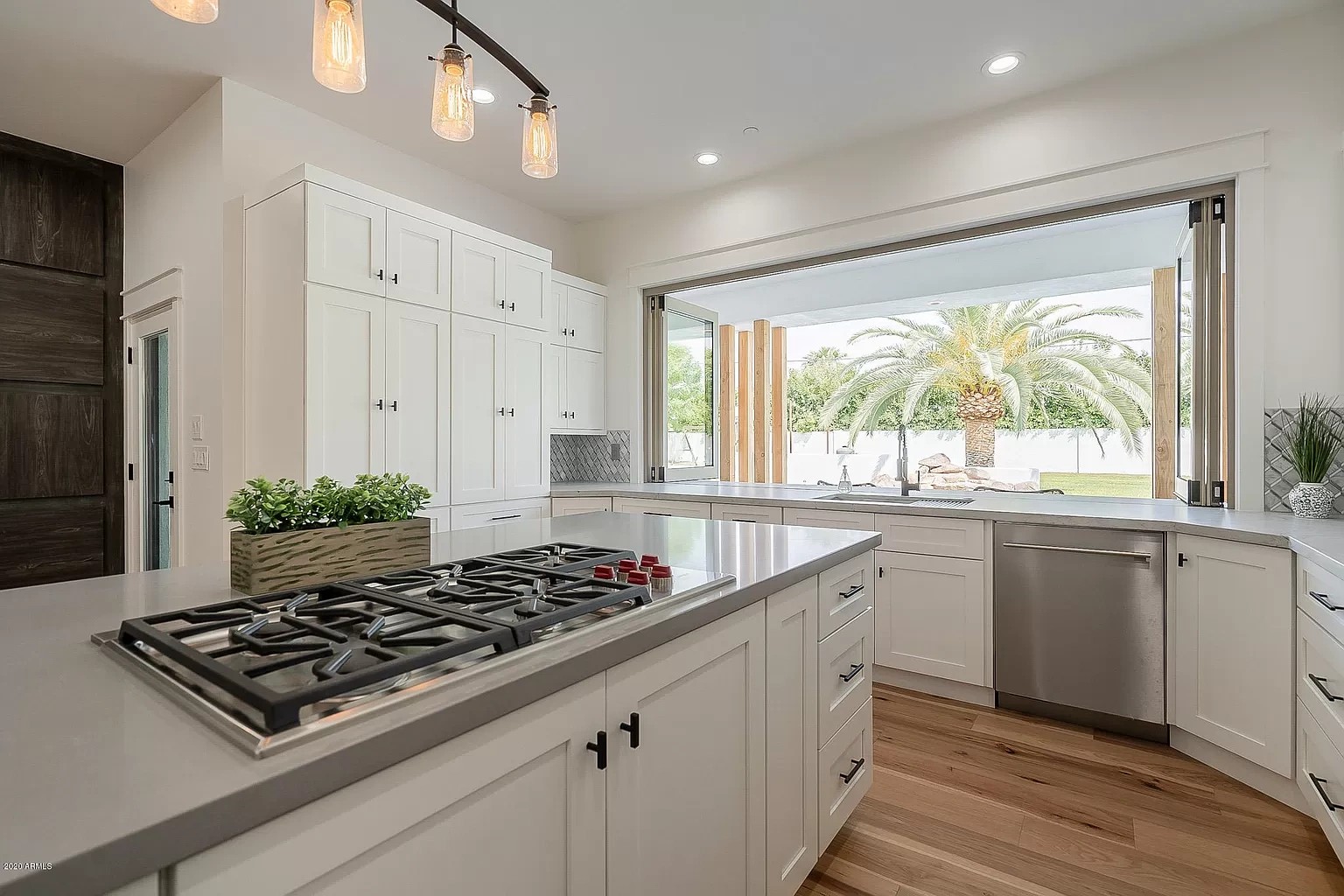 White kitchen with grey quartz counters and a folding window wall opened onto a palm-shaded yard