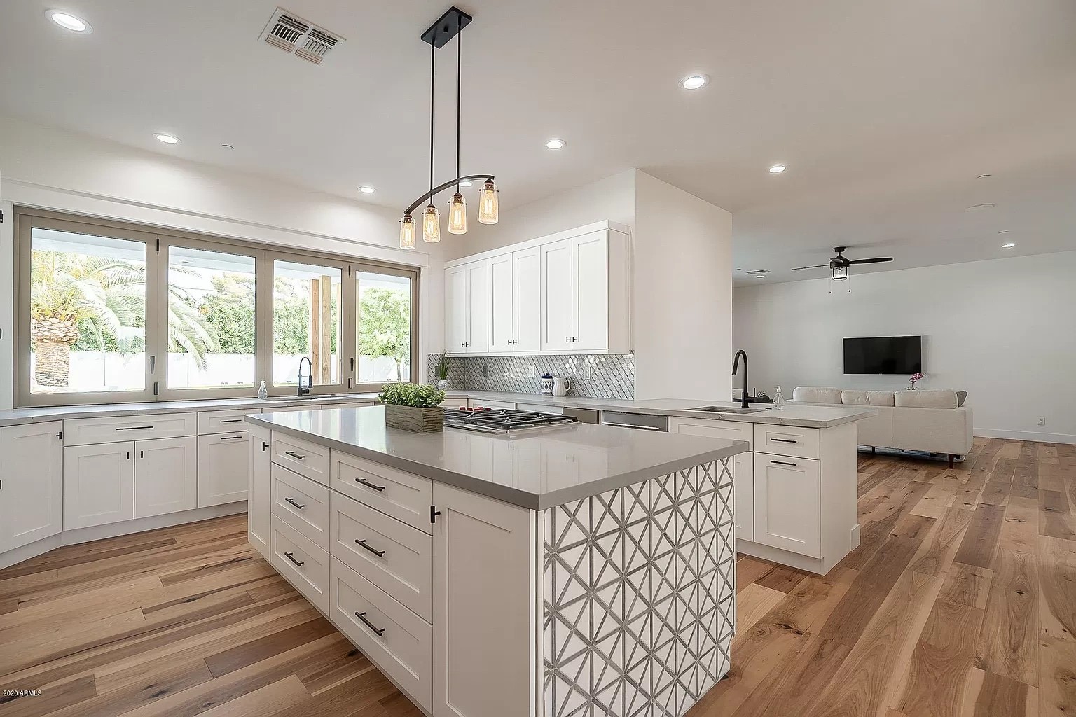 Open-plan white kitchen with a grey quartz island, patterned tile facing and wide plank floors