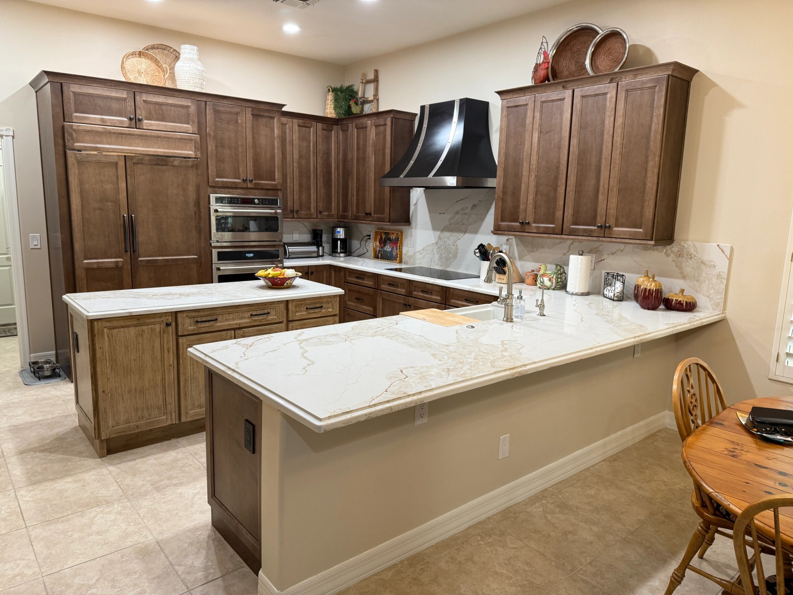 Stained maple kitchen with a quartz peninsula, wall ovens and a black range hood